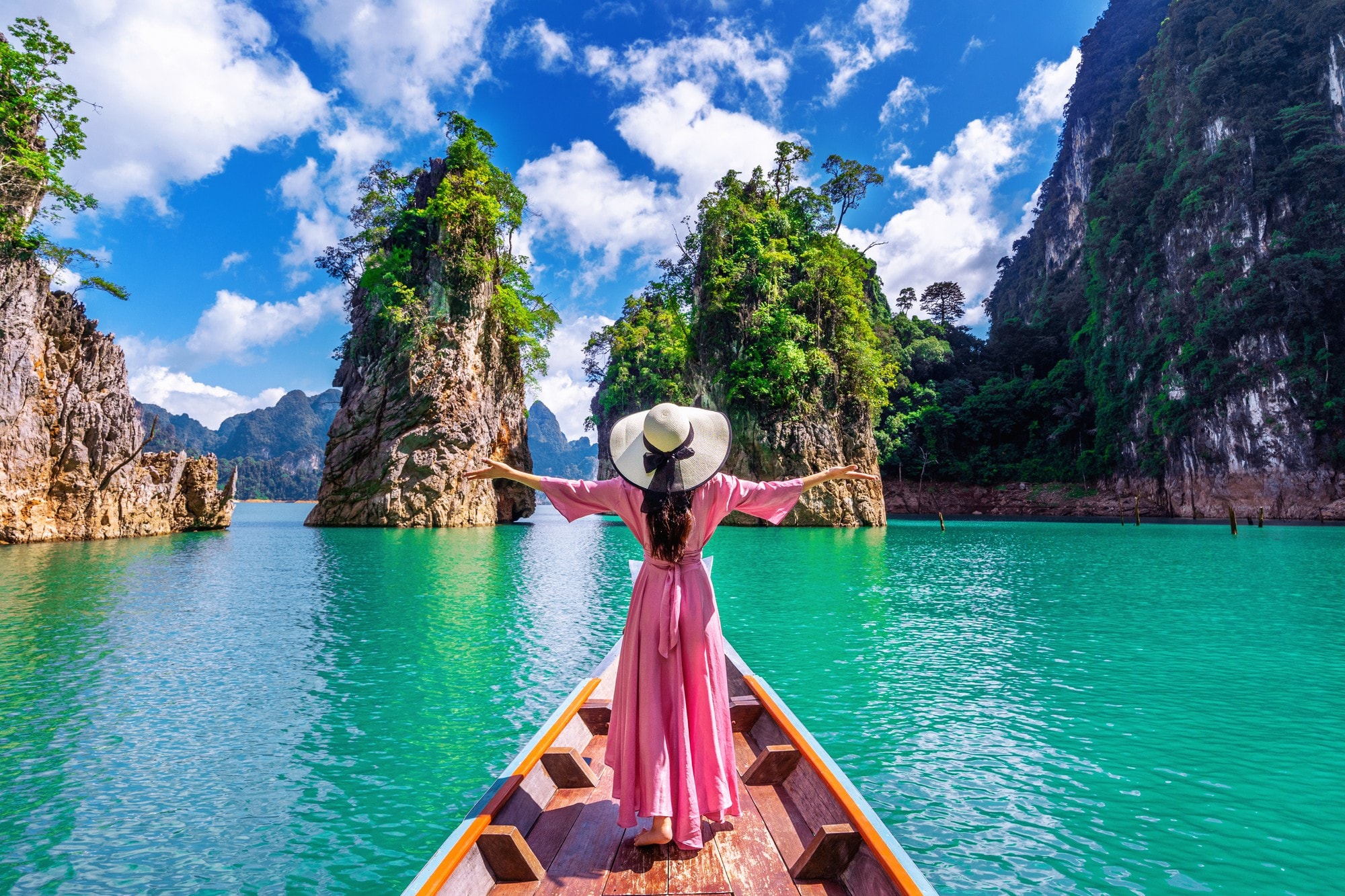 A traveller in a pink dress and sun hat on a longtail boat between green limestone cliffs