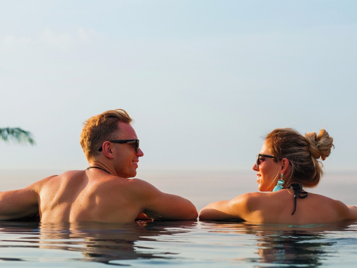 A couple relaxing at the edge of an infinity pool and smiling at each other