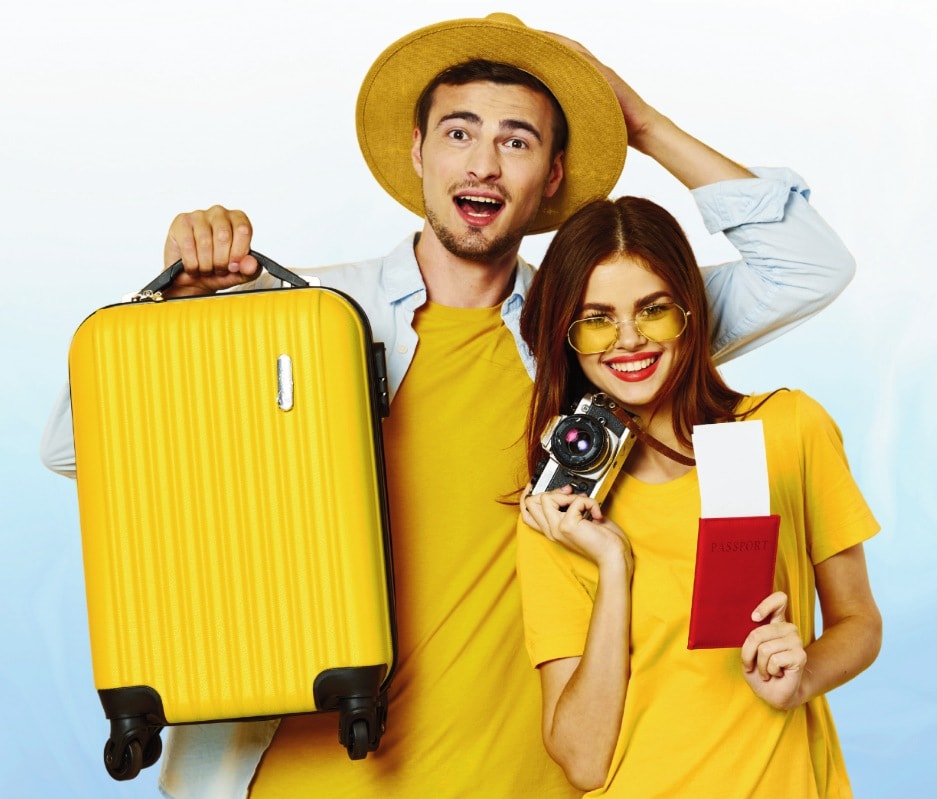 A smiling couple in yellow with a suitcase, camera and passport, ready to travel